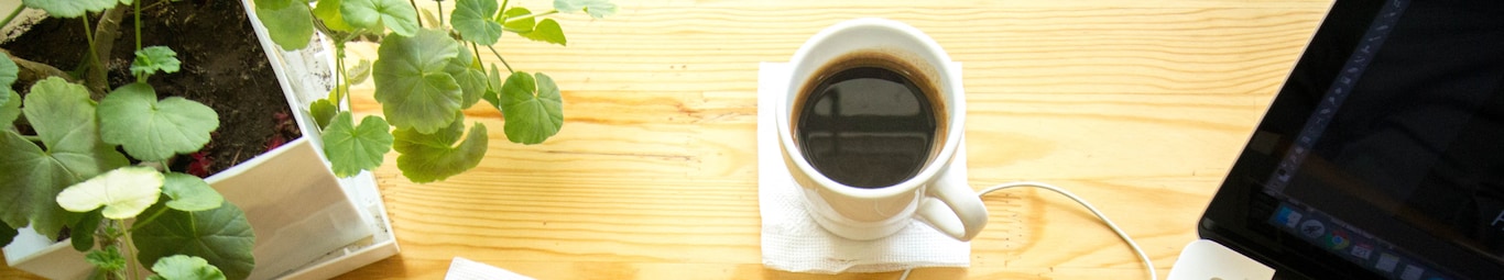 ceasca de cafea pe birou alaturi de o planta