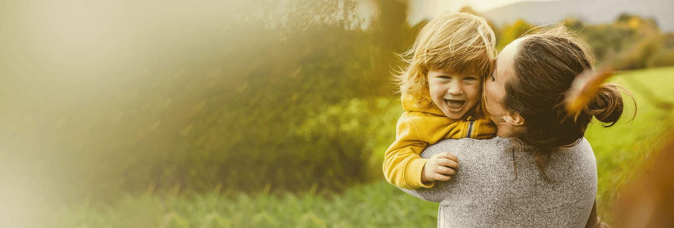 fetita blonda imbracata in galben este tinuta in brate de mama ei si pupata pe obraz