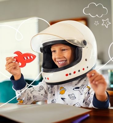 copil cu casca de astronaut are nava spatiala de lemn rosie in mana