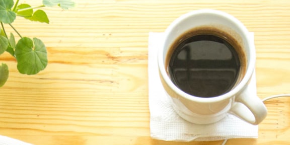 ceasca de cafea pe birou alaturi de o planta