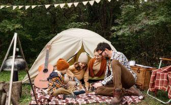 familie pe o paturica de picnic intr-o zi de toamna cu cortul in spate si o chitara alaturi