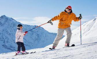 tatic cu o geaca galbena la ski cu baietelul pe o creasta montana acoperita cu zapada 
