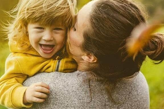 fetita blonda imbracata in galben este tinuta in brate de mama ei si pupata pe obraz