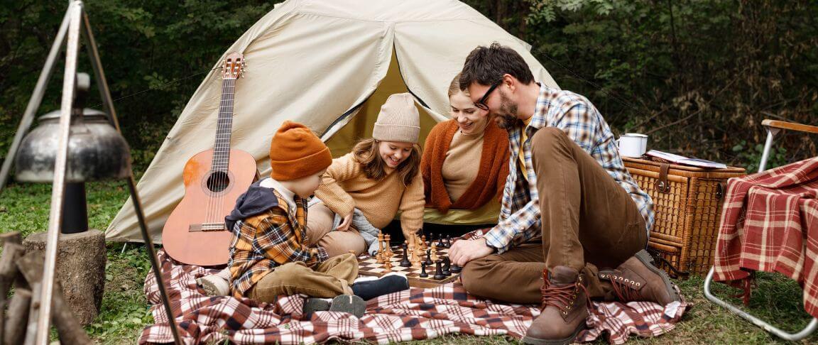 familie pe o paturica de picnic intr-o zi de toamna cu cortul in spate si o chitara alaturi