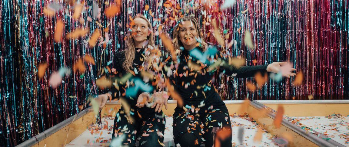doua femei vesele inconjurate de confetti la o petrecere